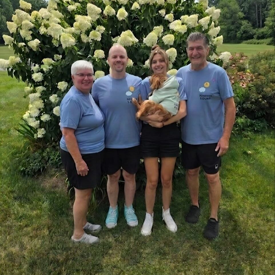 Four of our team in matching blue sunshine shirts in front of a blooming hydrangea, one of them holding Teddy in a mint-green hoodie