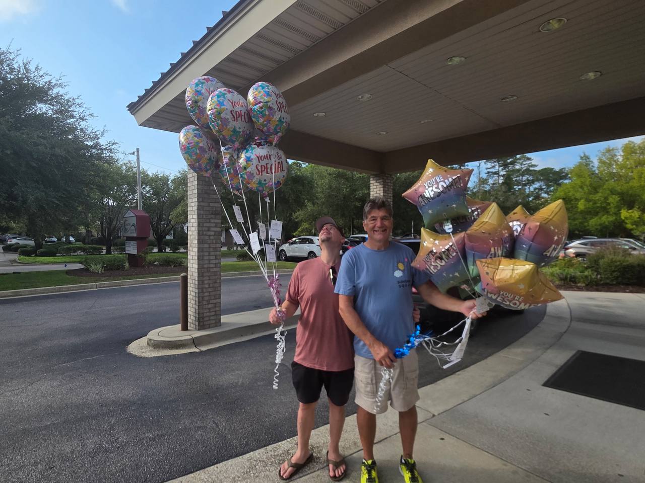 Jim and Chance hold balloon bouquets with cards attached outside the cancer center entrance.