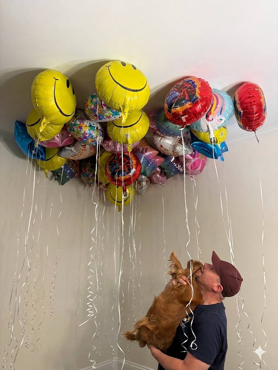 Chance holds Teddy the dog as they look up at a colorful cluster of balloons gathered on the ceiling.