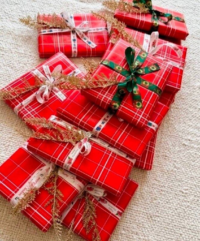 A pile of gifts wrapped in red plaid Christmas paper with ribbons and gold glitter sprigs.