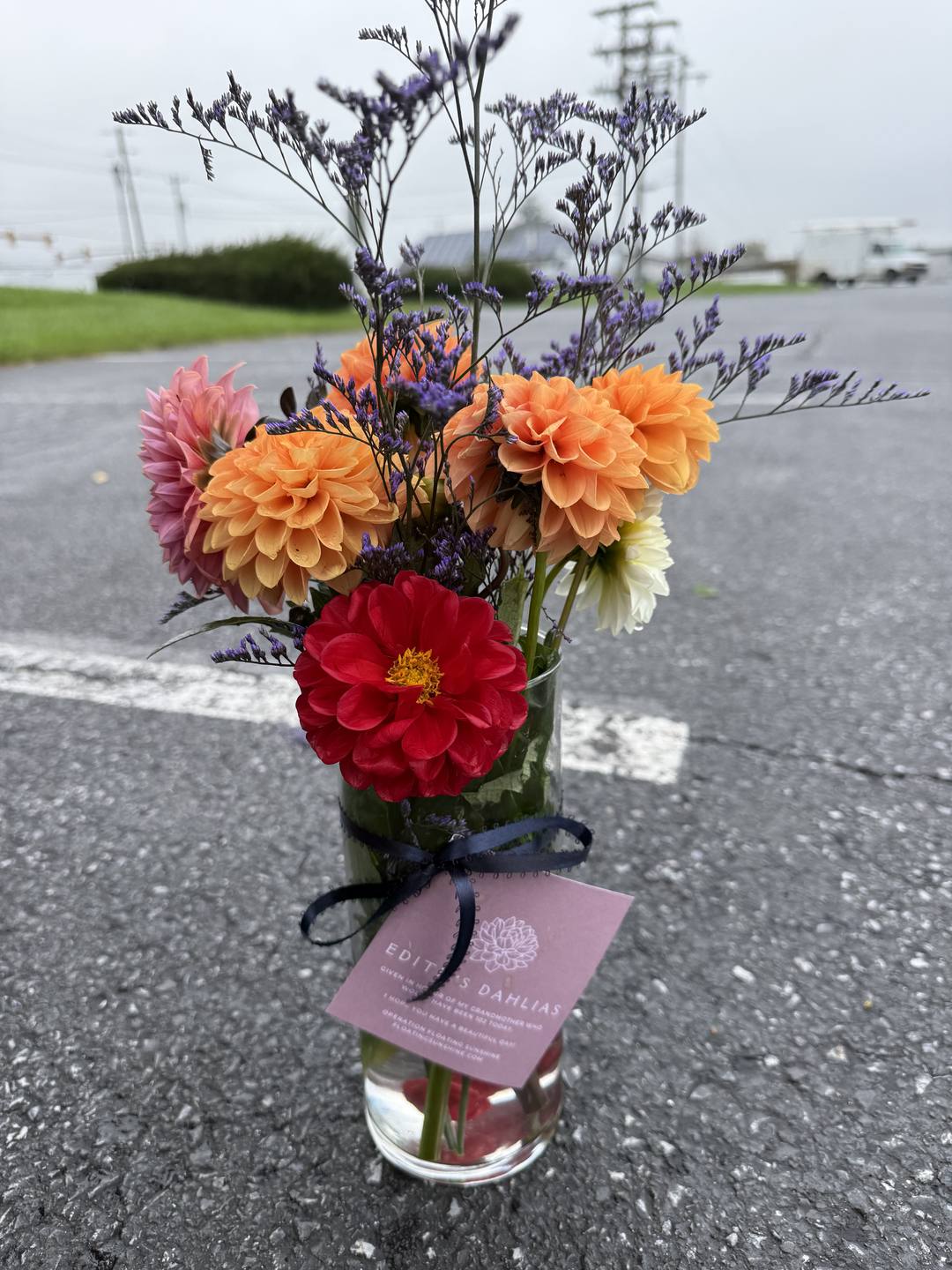 A finished bouquet of red, orange, and pink dahlias in a glass vase with a navy bow and an Edith's Dahlias tag.