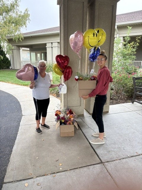 Ashton and her mom Chris stand outside the retirement community with a box of bouquets and bunches of heart and smiley-face balloons.