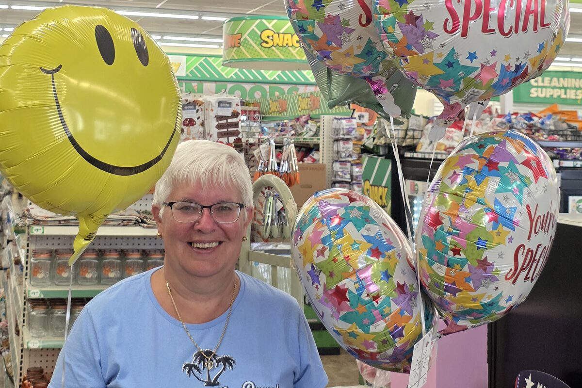 A smiling person surrounded by yellow smiley-face and colorful star-patterned balloons being prepared for delivery.