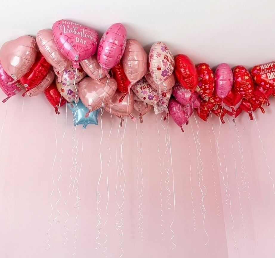 Dozens of pink and red heart-shaped Valentine's balloons floating against a ceiling with ribbons hanging down.
